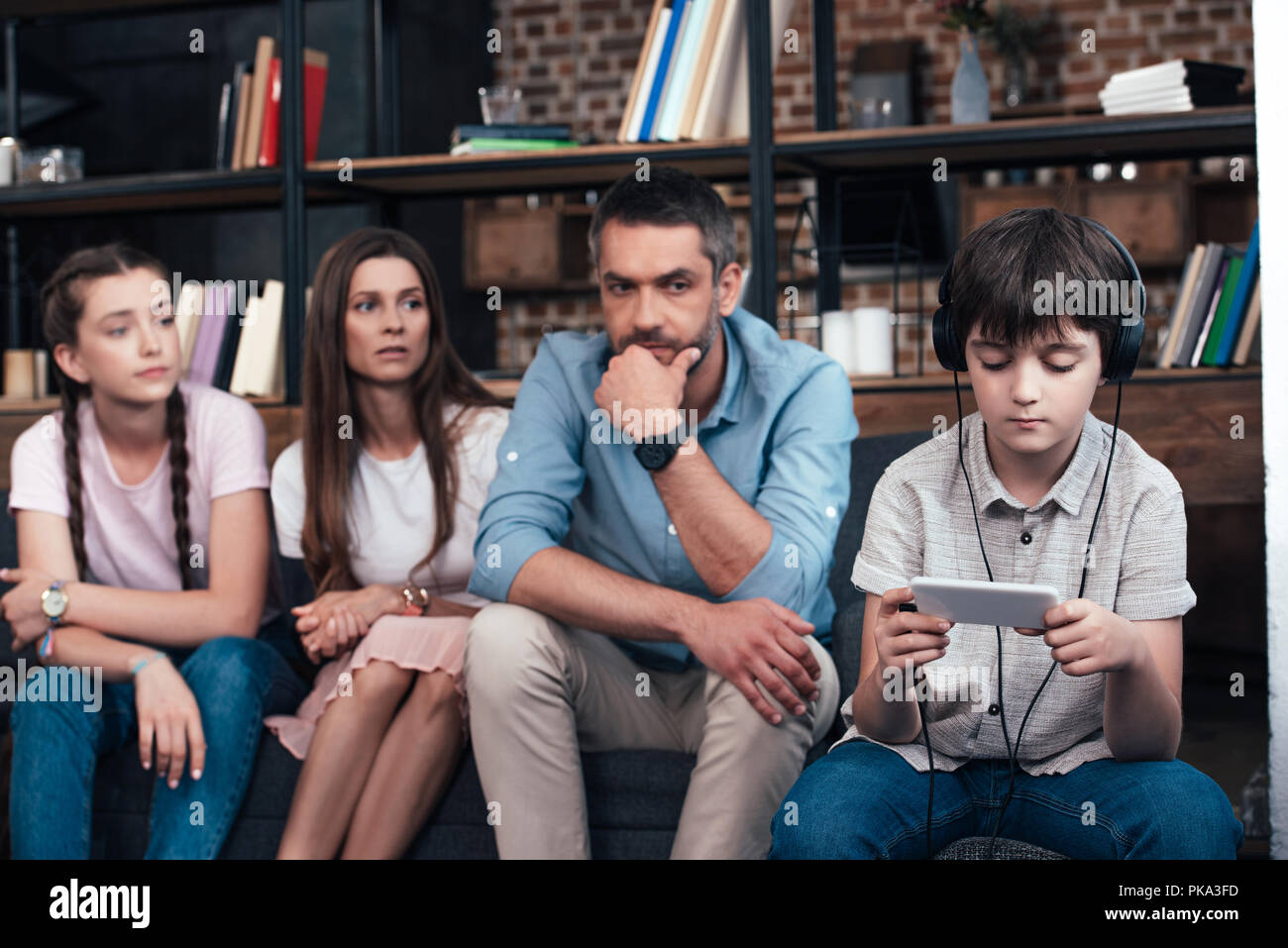 Parents et sa sœur à la dépendance à l'aide d'écouteurs en garçon sur smartphone session de thérapie familiale Banque D'Images