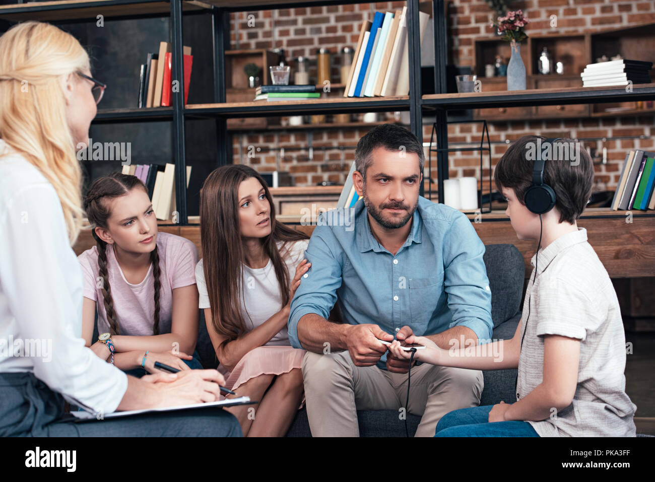 Père enlève le smartphone de fils dans le casque sur la thérapie familiale session par conseillère in office Banque D'Images