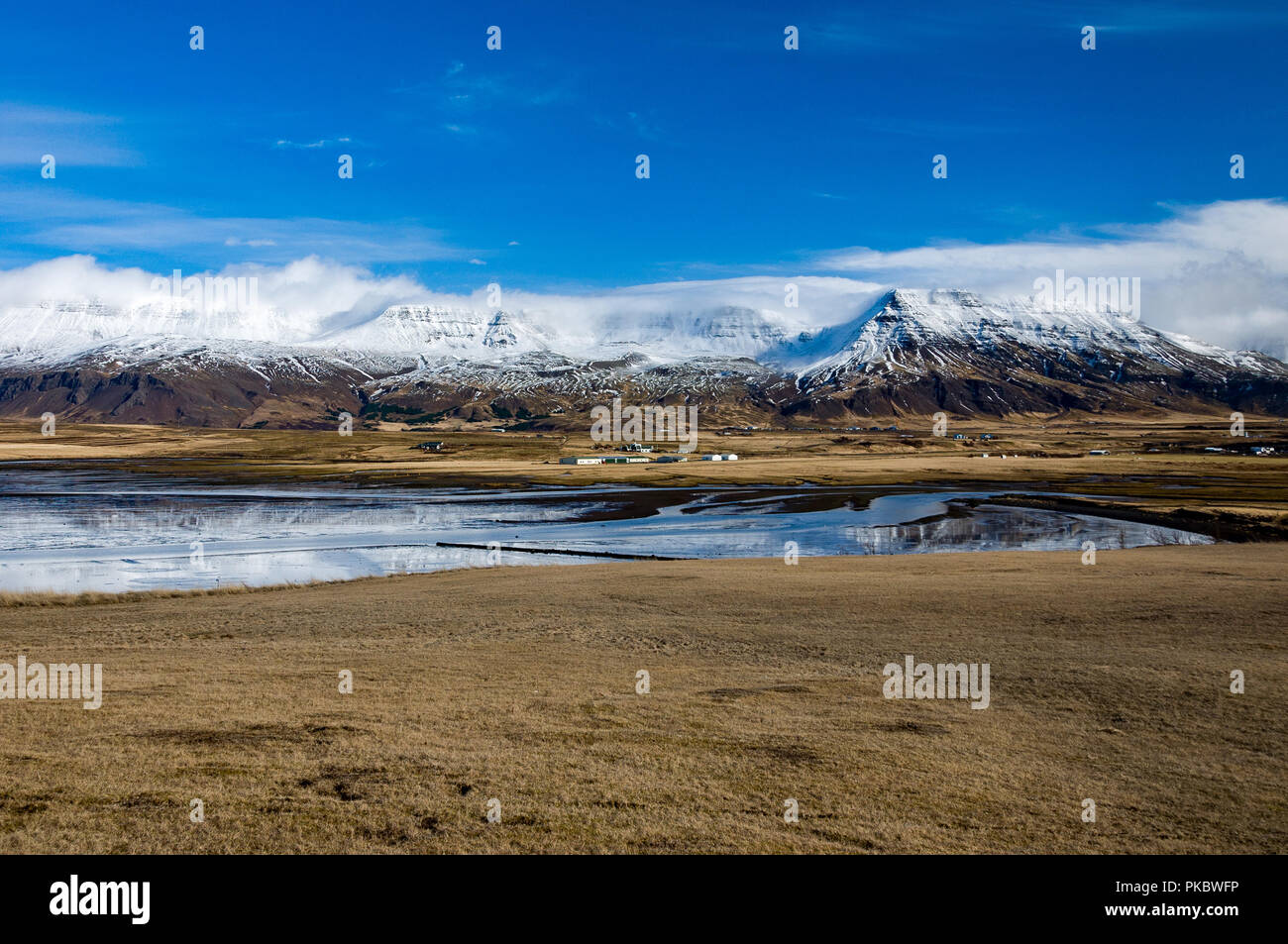 Nuage de neige et de montagnes enneigées à côté d'herbage, maisons et la mer à Leiruvogur Cove, l'Islande Banque D'Images