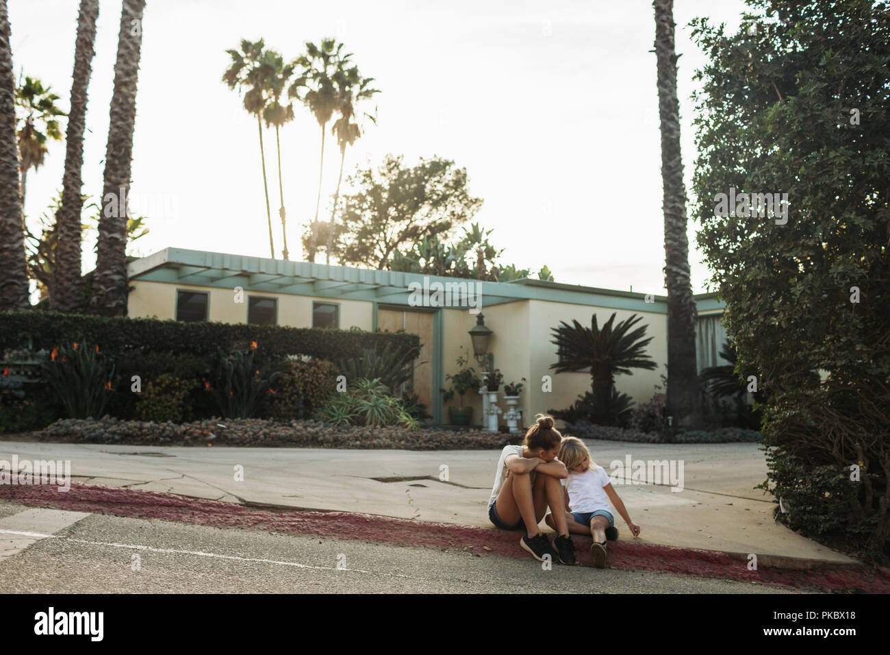 Deux jeunes filles s'asseoir sur un trottoir de la rue à l'extérieur d'une maison, Los Angeles, Californie, États-Unis d'Amérique Banque D'Images