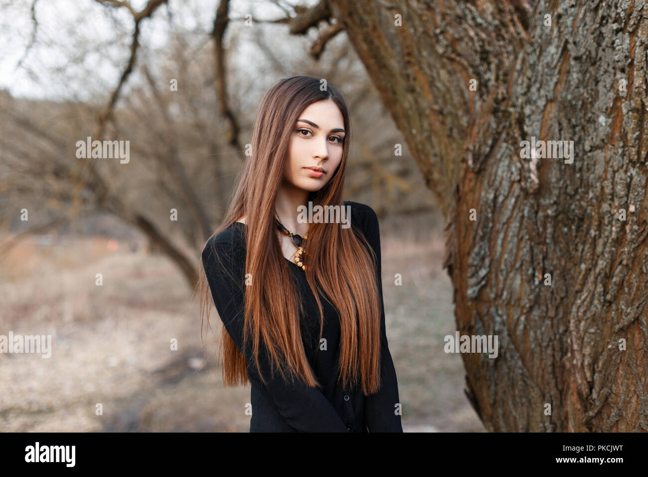 Belle jeune fille au chemisier noir sur un arrière-plan du parc. Au début du printemps Banque D'Images