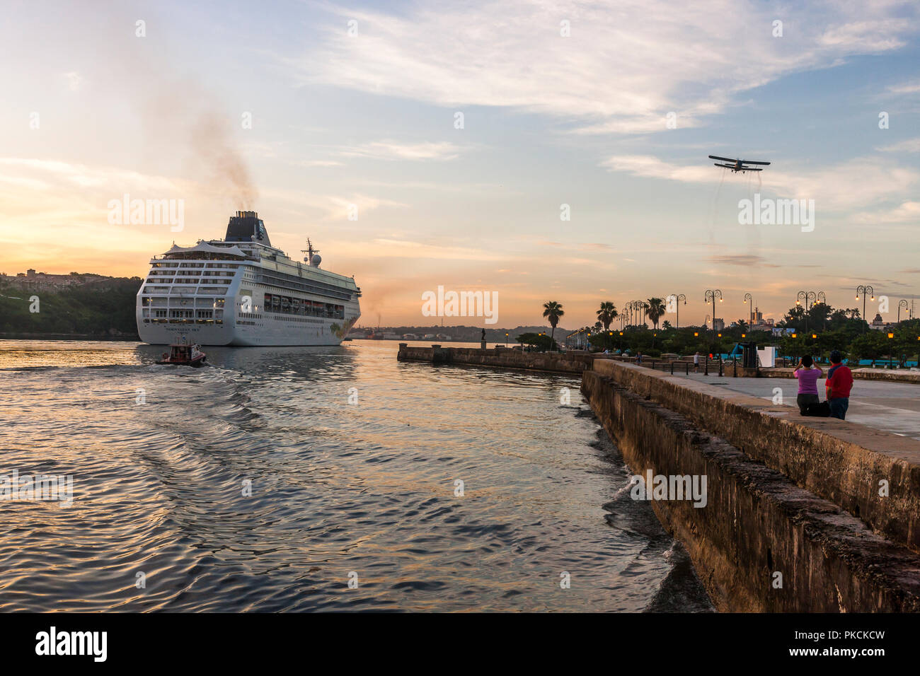 La Havane, Cuba. Le 04 juillet 2017. Bateau de croisière Norwegian Sky fait son chemin jusqu'à son dock escorté par le bateau-pilote tandis qu'un vieux millésime d'un biplan vole ov Banque D'Images