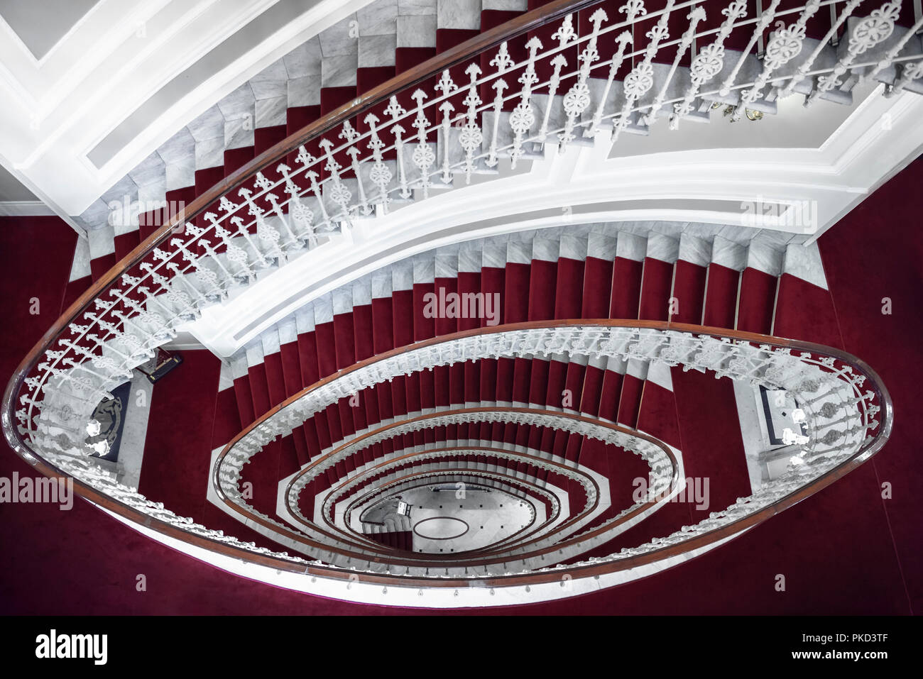 La symétrie de l'architecture avec un élégant escalier en spirale, vue ci-dessus, fait de marbre blanc et recouvert de tapis rouge, dans un hôtel à Gênes, en Italie. Banque D'Images