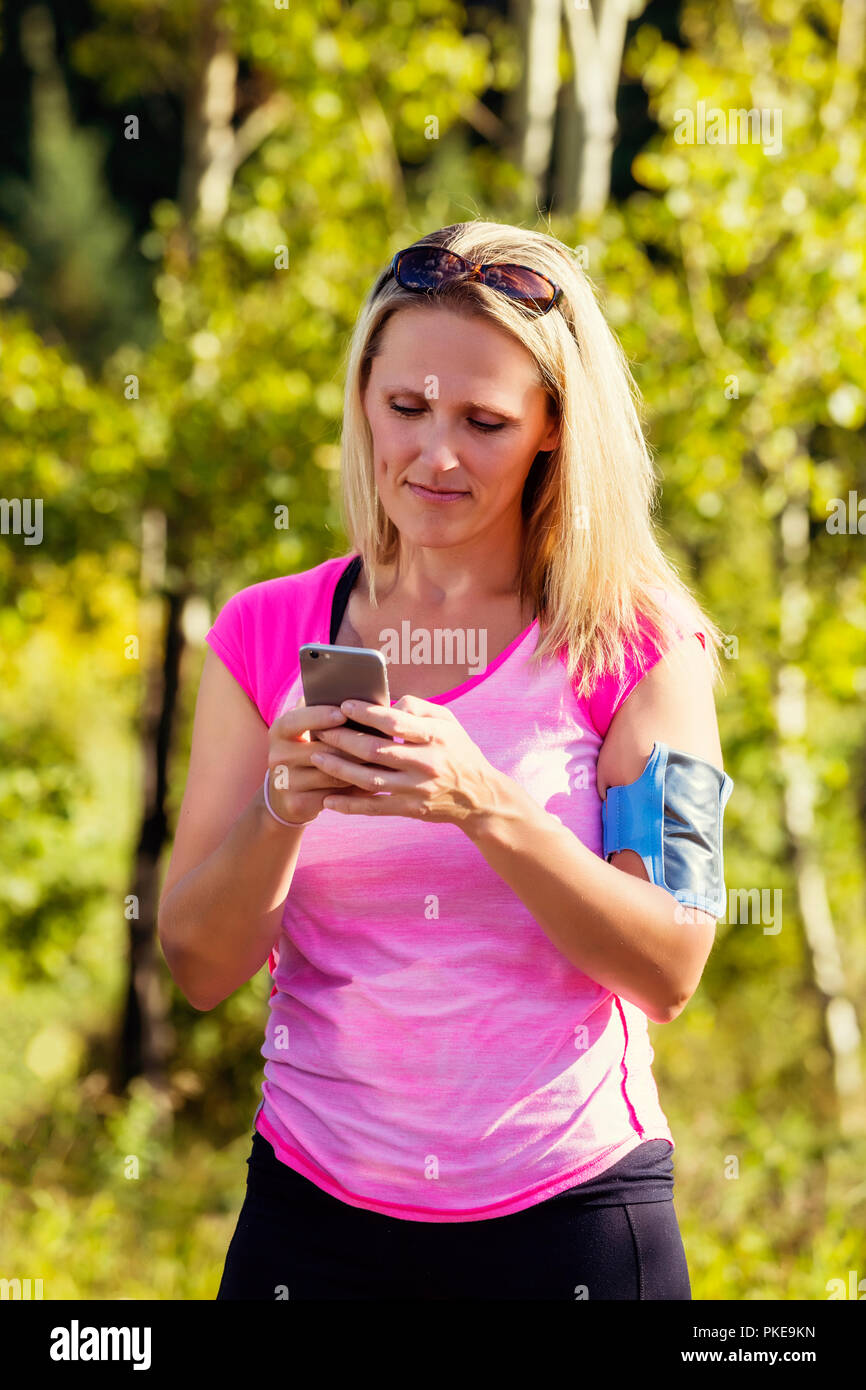 A young woman wearing active wear et un brassard de tenir son téléphone intelligent de textes avant de partir pour une course dans un parc de la ville pendant la saison d'automne Banque D'Images