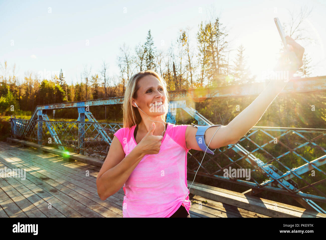Une femme portant des vêtements et un brassard pour son téléphone portable se tient sur un pont dans un parc en automne en prenant un auto-portrait avec son téléphone portable Banque D'Images