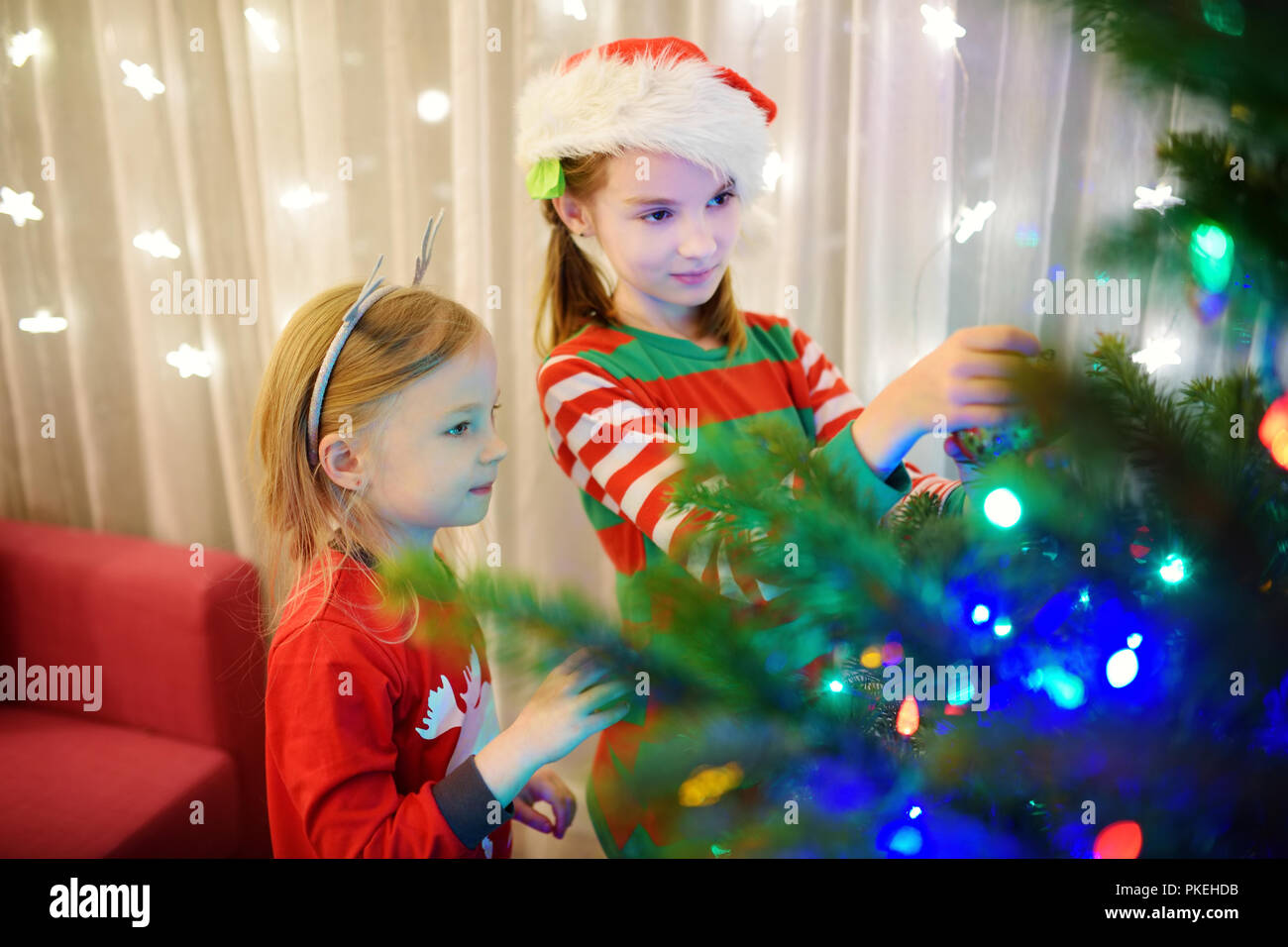 Deux adorables sœurs décorer un arbre de Noël avec boules en verre coloré à la maison. Loisirs en famille au moment de Noël merveilleux. Découpage d'un arbre de fête. Banque D'Images