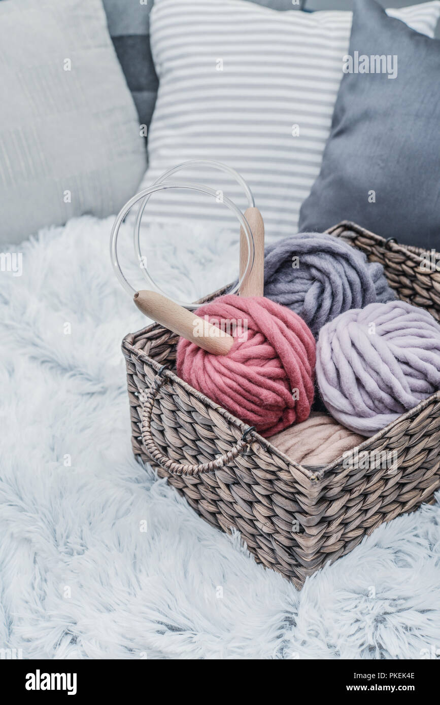 Boules de fil de laine merino chunky super avec des aiguilles dans le panier rustique sur fond de fourrure blanche pelucheuse. Banque D'Images