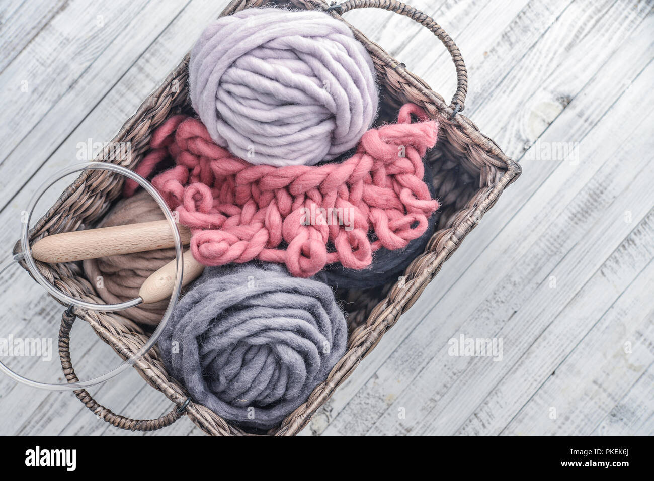 Boules de fil de laine merino chunky super avec des aiguilles dans le panier rustique sur fond bleu clair. Banque D'Images