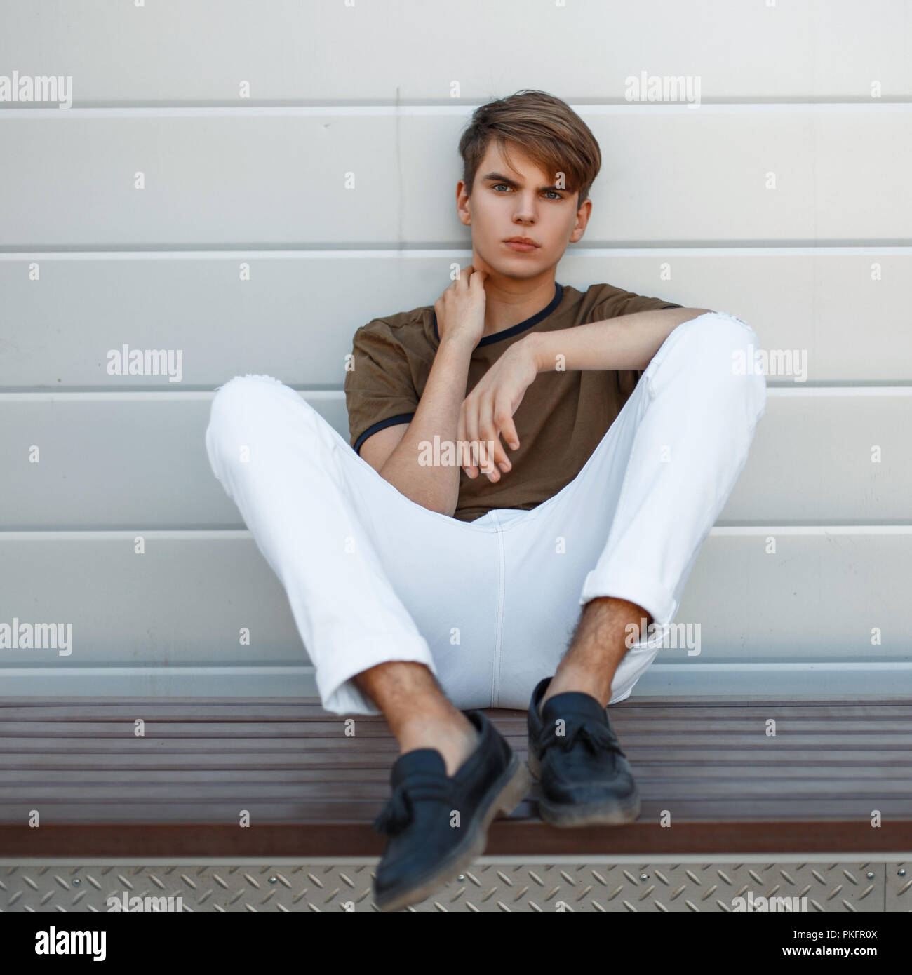 Jeune homme en T-shirt et pantalon blanc avec des chaussures noires en cuir  se trouve près de la paroi métallique Photo Stock - Alamy