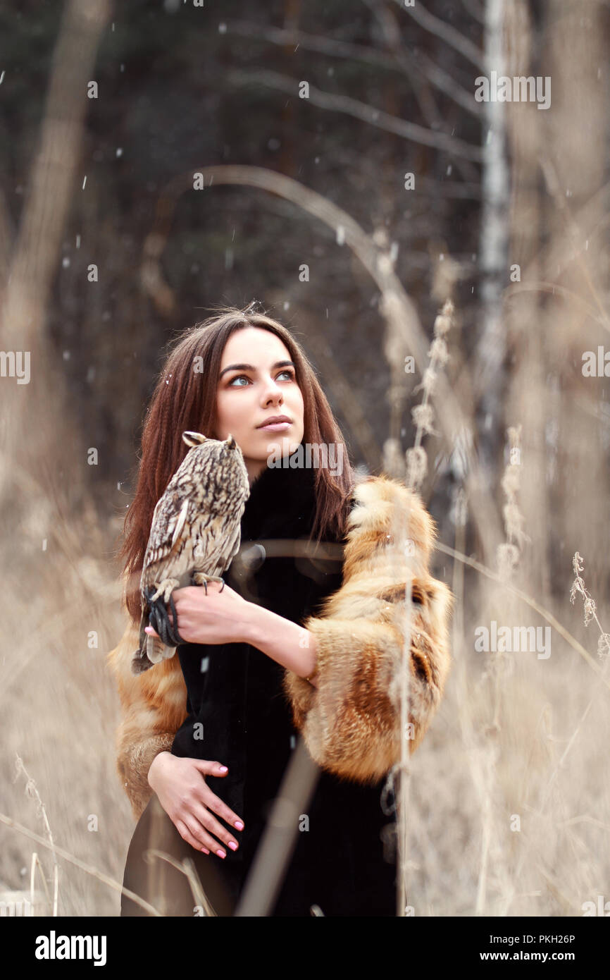 Femme en manteau de fourrure avec owl sur la main en première neige  d'automne. Belle brune aux cheveux longs dans la nature, la tenue d'un  hibou. Regarder les filles romantique et délicate