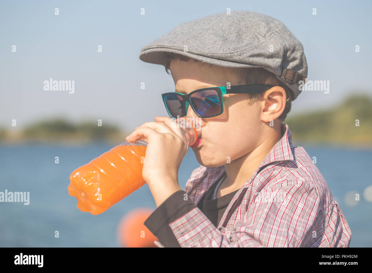 Close up portrait of a cute little boy avec un chapeau et des lunettes de  soleil, assis au bord de l'eau, boire du jus et profiter de la belle  journée ensoleillée Photo