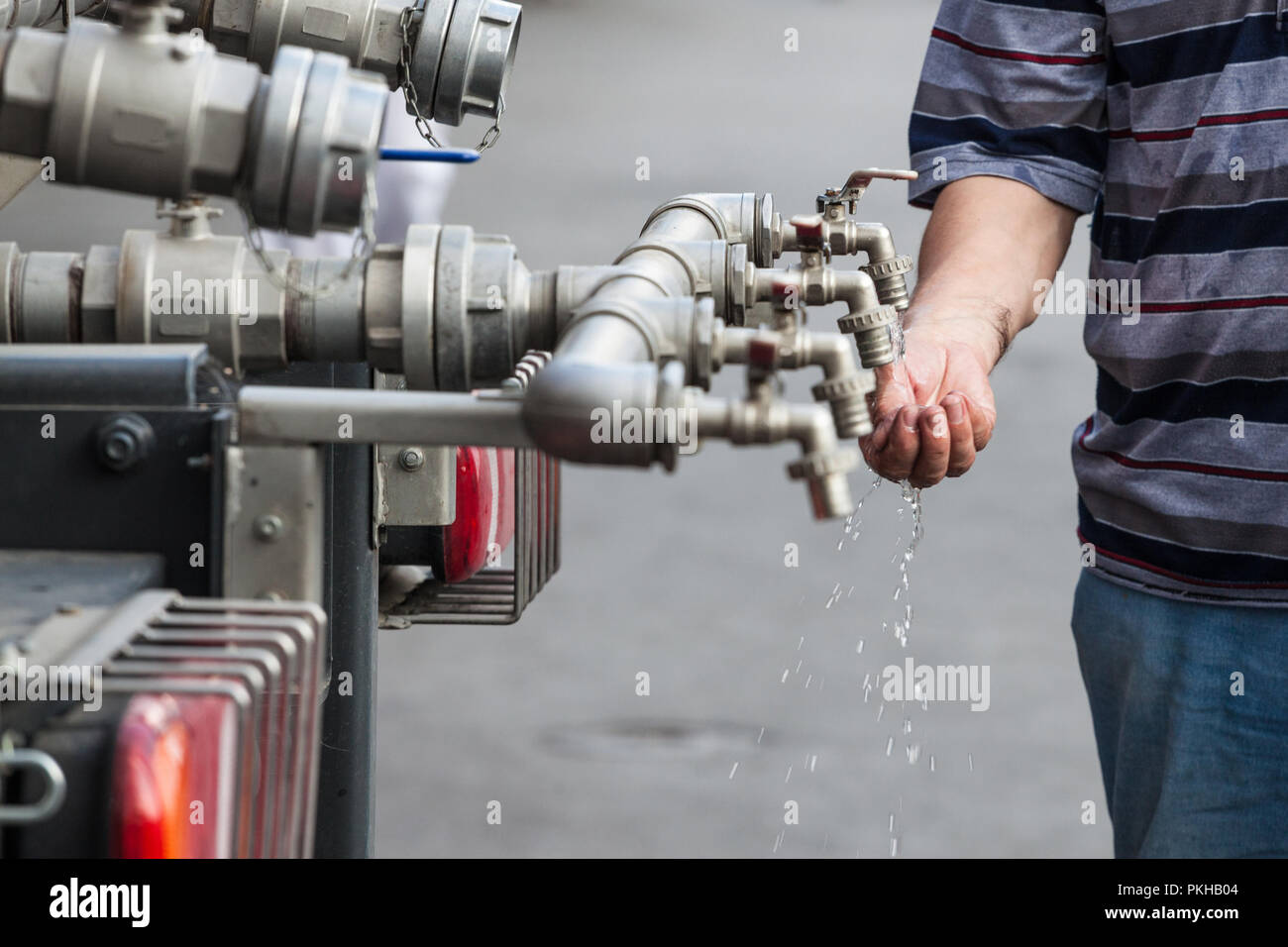 Un robinet d'eau composé de plusieurs tuyaux, avec les mains essayant de retenir l'eau pour l'enregistrer et le boire. Ce robinet distribue à un public de l'eau potable propre Pi Banque D'Images