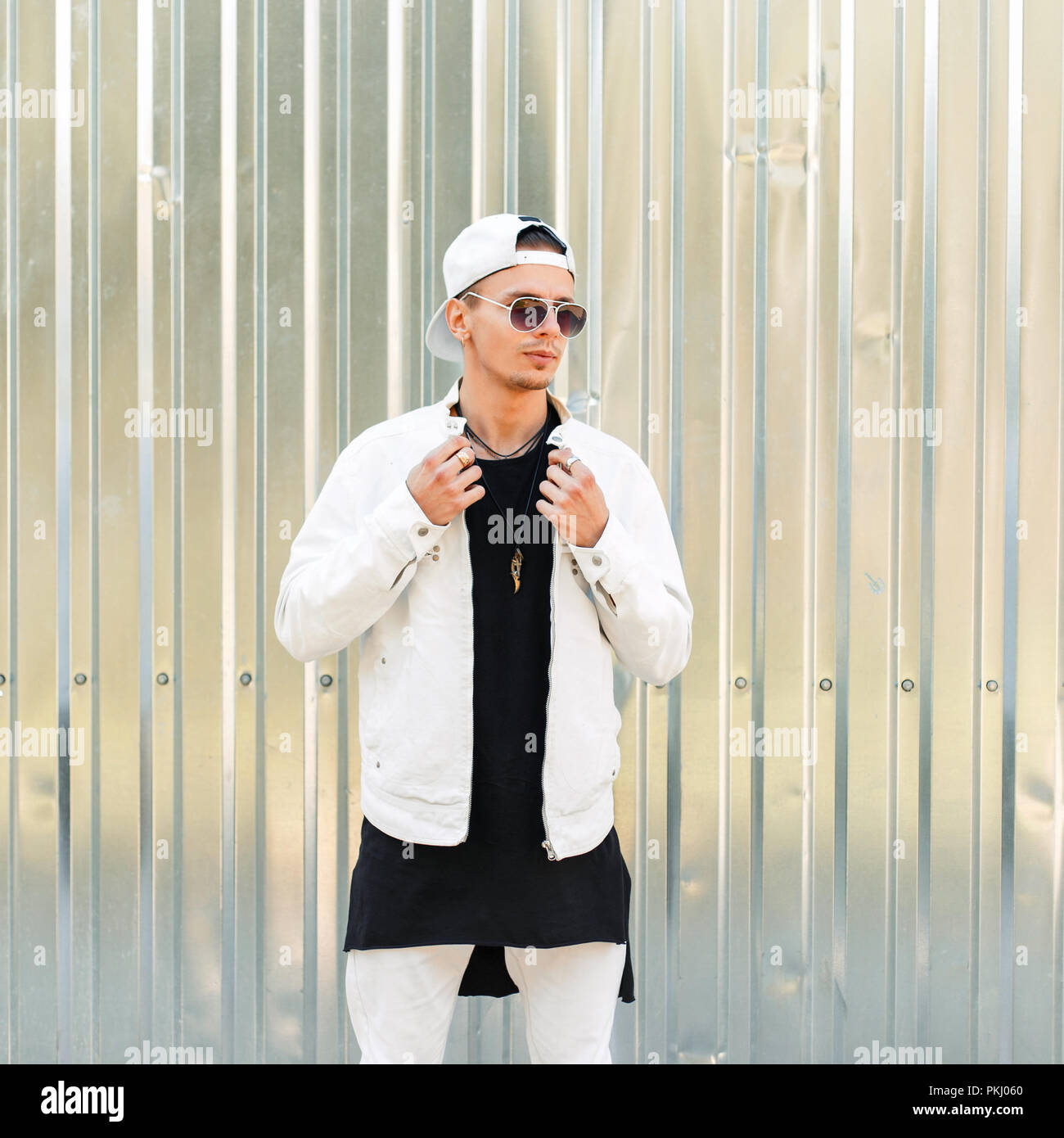 Bel homme élégant avec des lunettes de soleil dans une veste blanche avec  une casquette de baseball près de la paroi métallique Photo Stock - Alamy