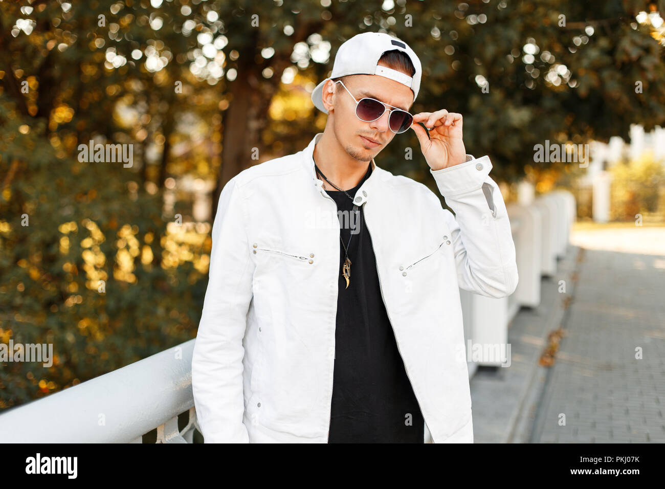 Bel homme à la mode de lunettes de soleil dans une veste blanche avec une  casquette de baseball sur la rue dans la journée d'automne Photo Stock -  Alamy