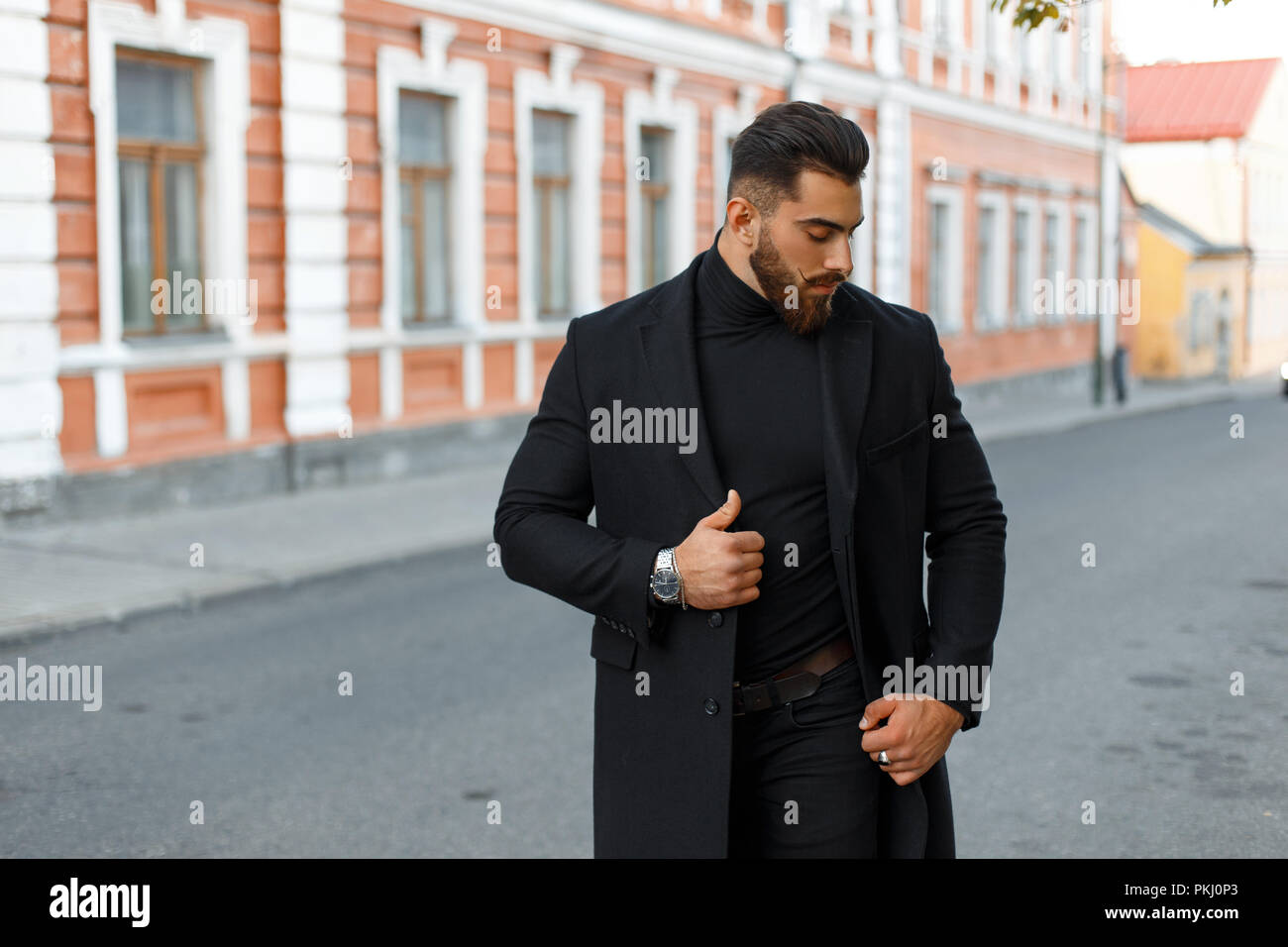 Bel homme fort élégant dans un manteau à la mode noir marche sur la rue  Photo Stock - Alamy