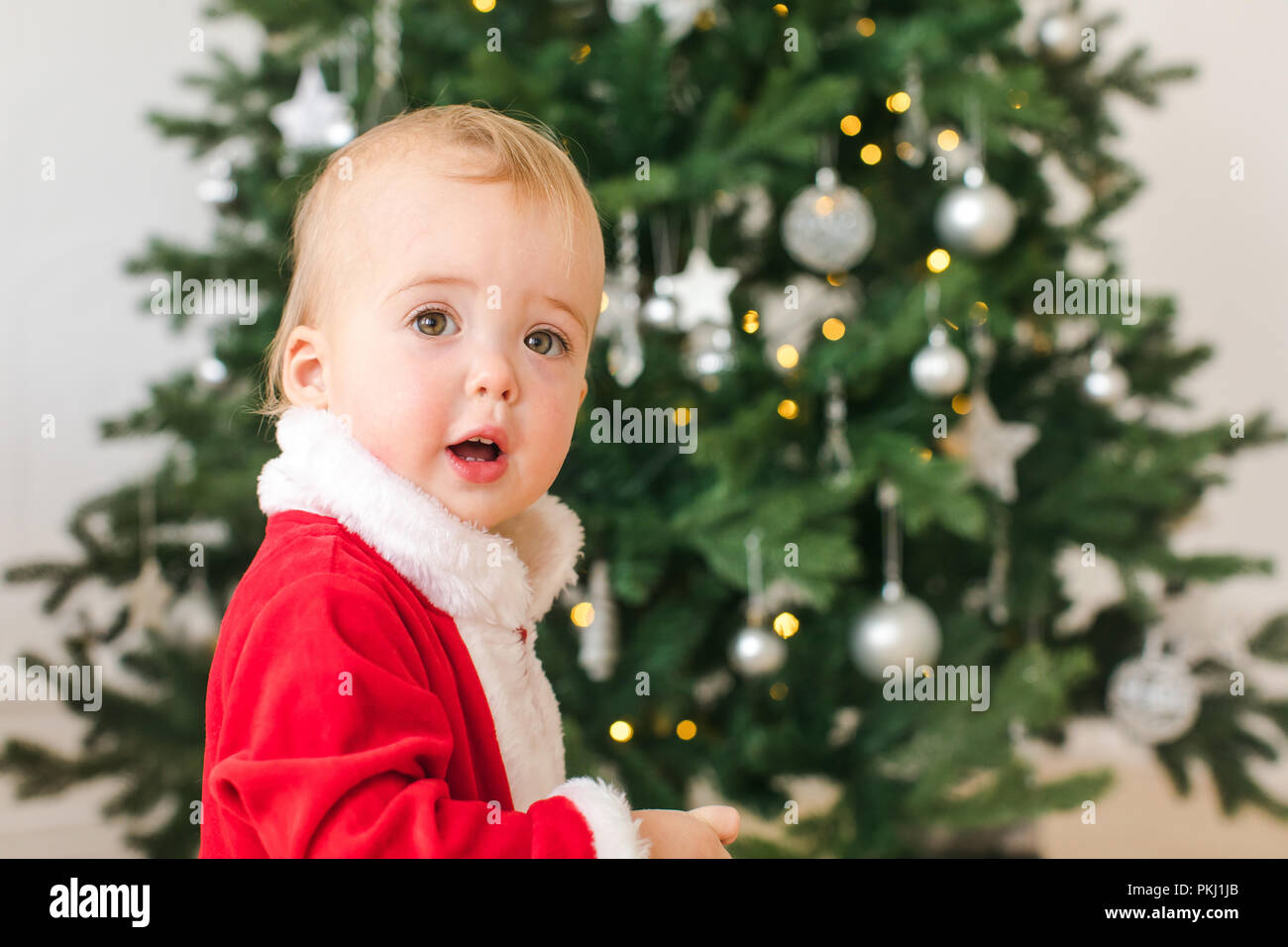 Petit garçon en costume de Père Noël, debout près de l'arbre de Noël Banque D'Images