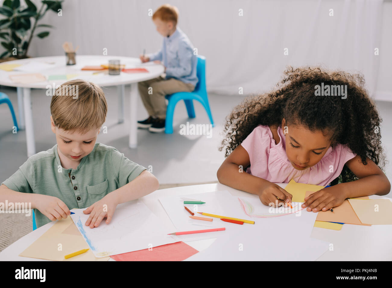 Les enfants d'âge préscolaire multiculturelle des dessins avec des crayons en classe Banque D'Images