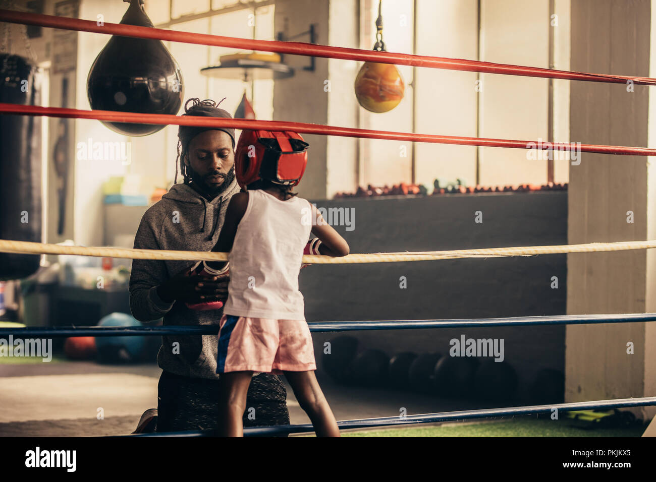 Vue arrière d'un boxing enfants parler à son entraîneur se tenant debout à l'intérieur du ring. Kid boxing et garde la tête à l'intérieur d'un permanent rin boxe Banque D'Images