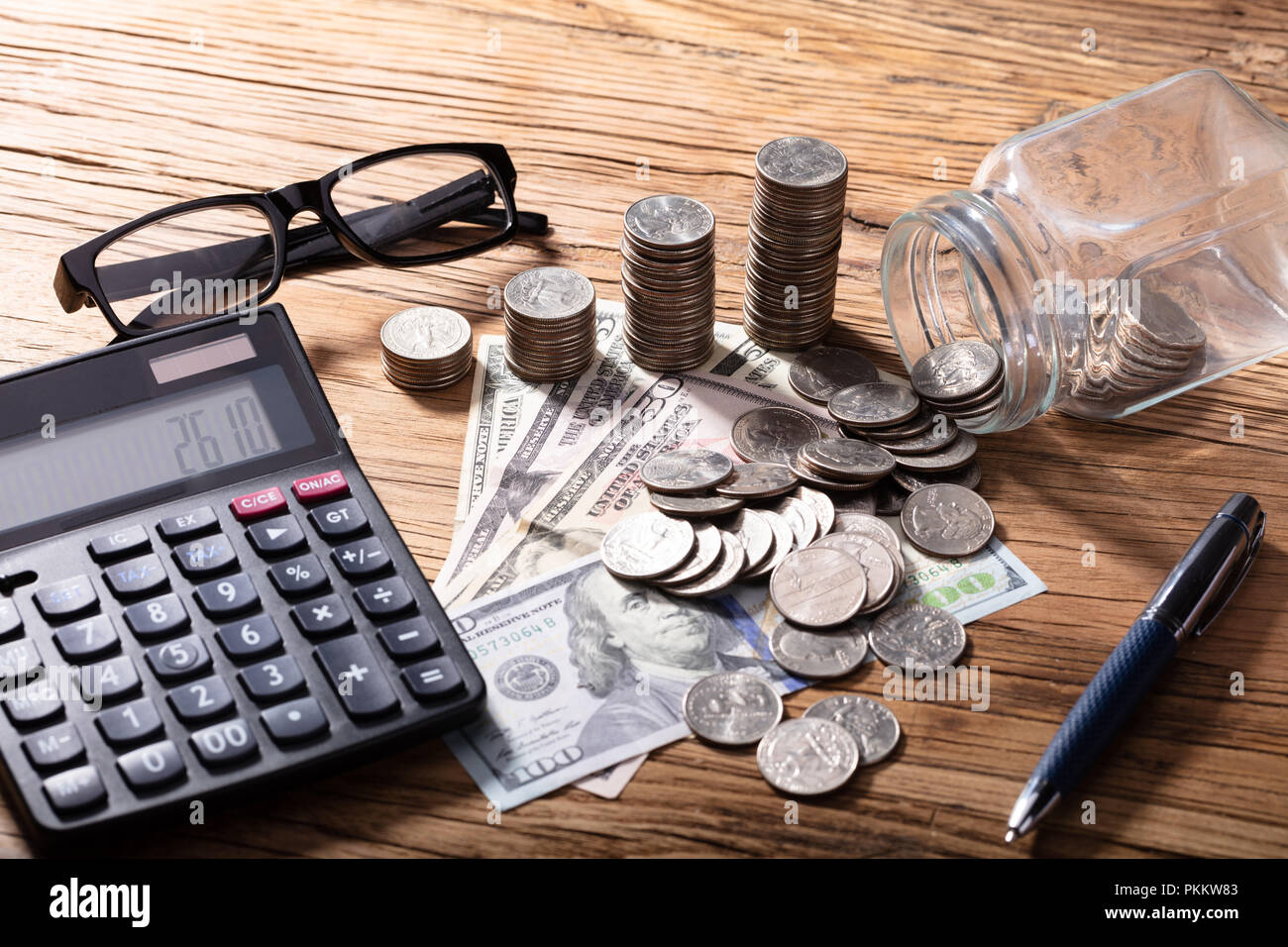 La pile de pièces et de billets avec la calculatrice sur table en bois Banque D'Images