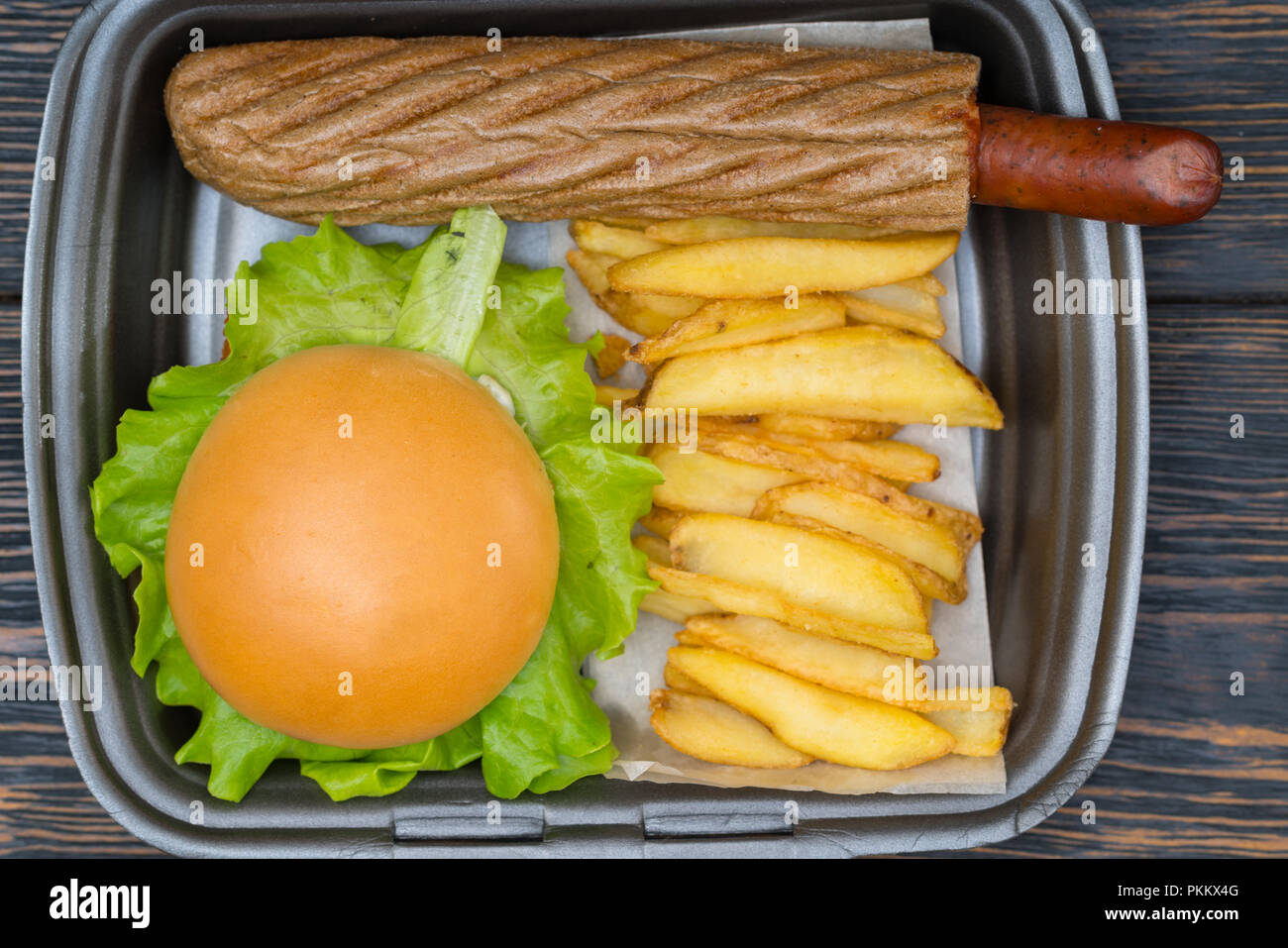 Vue aérienne sur noir contenant de burger assis à côté de tranches de pommes de terre et la chair à saucisses enveloppées dans du pain Banque D'Images