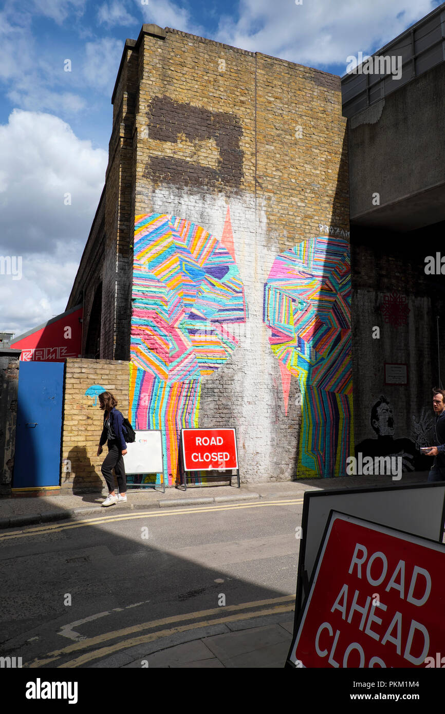 Jeune femme en passant devant un graffiti sur mur du bâtiment à New Inn Yard, Shoreditch East London UK KATHY DEWITT Banque D'Images