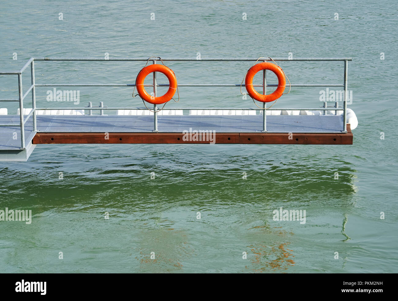 Jetée flottante avec bouées de sauvetage orange sur le Danube, équipement de sécurité simple au bord de la rivière au-dessus de l'eau verte calme. Banque D'Images