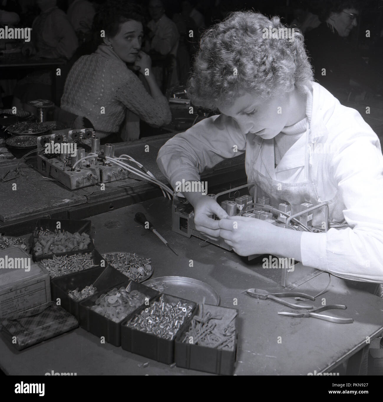 Années 1950, historique, un travailleur féminin assis à un banc de branchement à la main les composants électriques pour un tube à vide sans fil radio sur le sol de l'usine du fabricant électrique britannique Radio Bush, Londres, Angleterre. De nombreux emplois en usine effectuée auparavant par les hommes ont été prises en charge au cours de la DEUXIÈME GUERRE MONDIALE par des femmes et ils ont continué dans ces rôles dans l'après-guerre. Banque D'Images