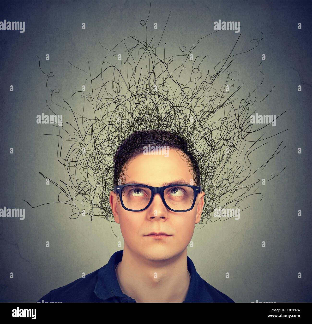 Jeune homme à lunettes avec les pensées dans l'anxiété et le chaos à la haut sur fond gris Banque D'Images