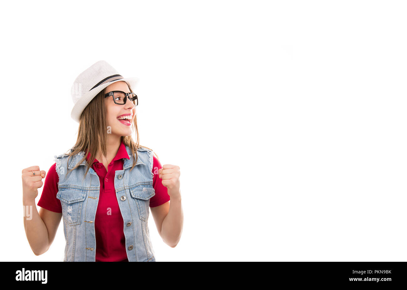 Casual young woman in hat et verres avec les poings en criant se sentir excité à la super heureux de le côté isolé sur fond blanc Banque D'Images