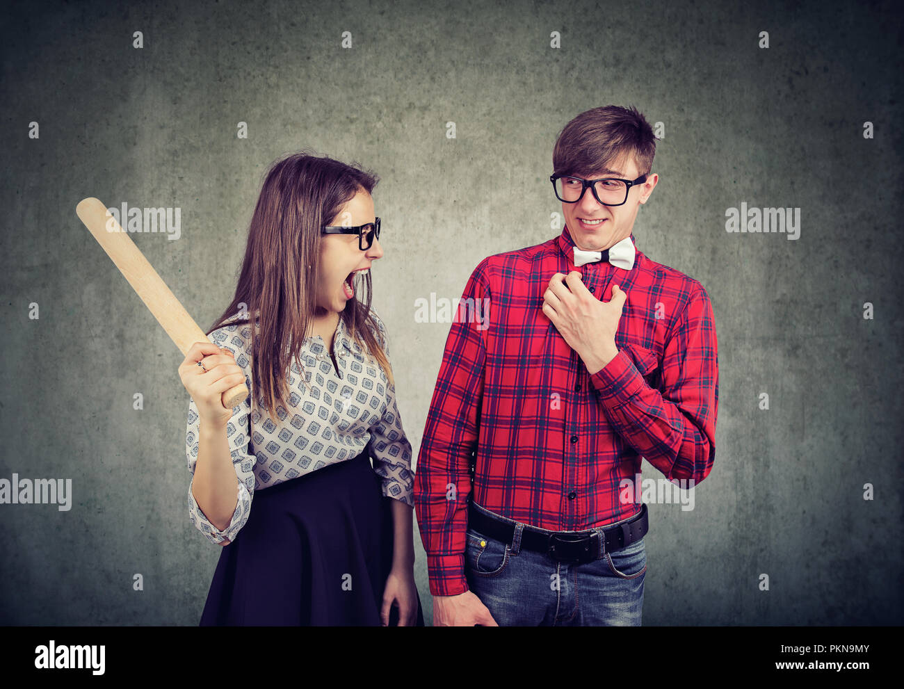 Jeune femme avec rouleau à pâtisserie à la folie tout en avançant avec l'homme sur fond gris Banque D'Images