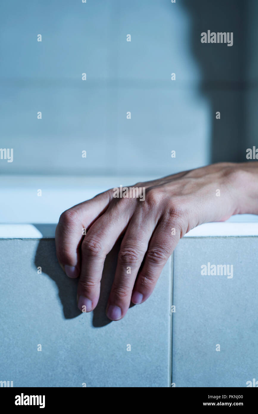 Libre de la main d'un jeune homme de race blanche sur le côté d'une baignoire, d'une atmosphère mystérieuse, avec un effet dramatique Banque D'Images