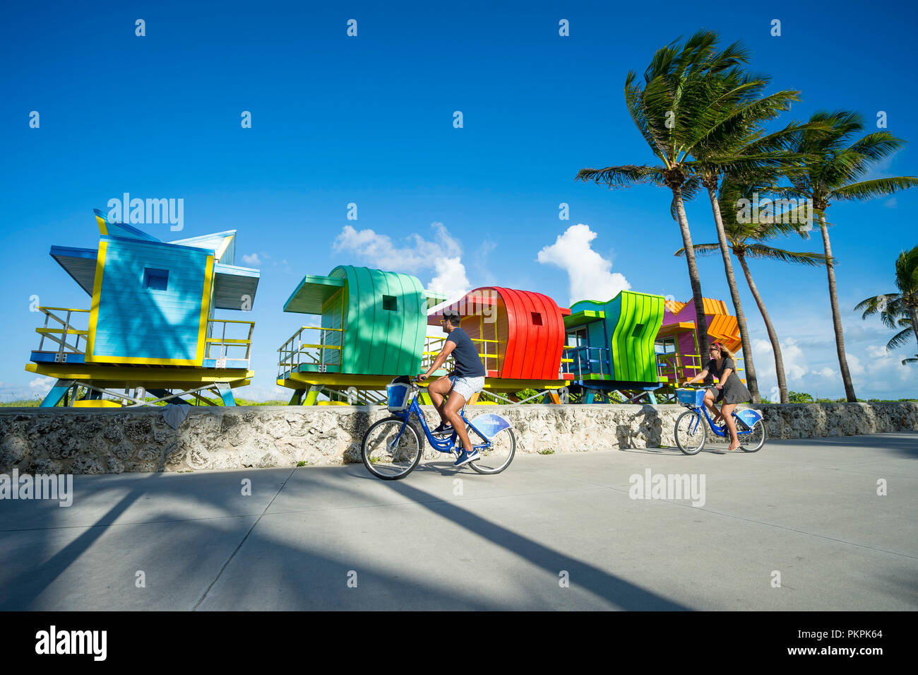 MIAMI - CIRCA Juillet 2017 : les touristes ride 'vélo' Citi location partager le long de la promenade de Miami Beach avec fond de tours de sauveteur et de palmiers Banque D'Images
