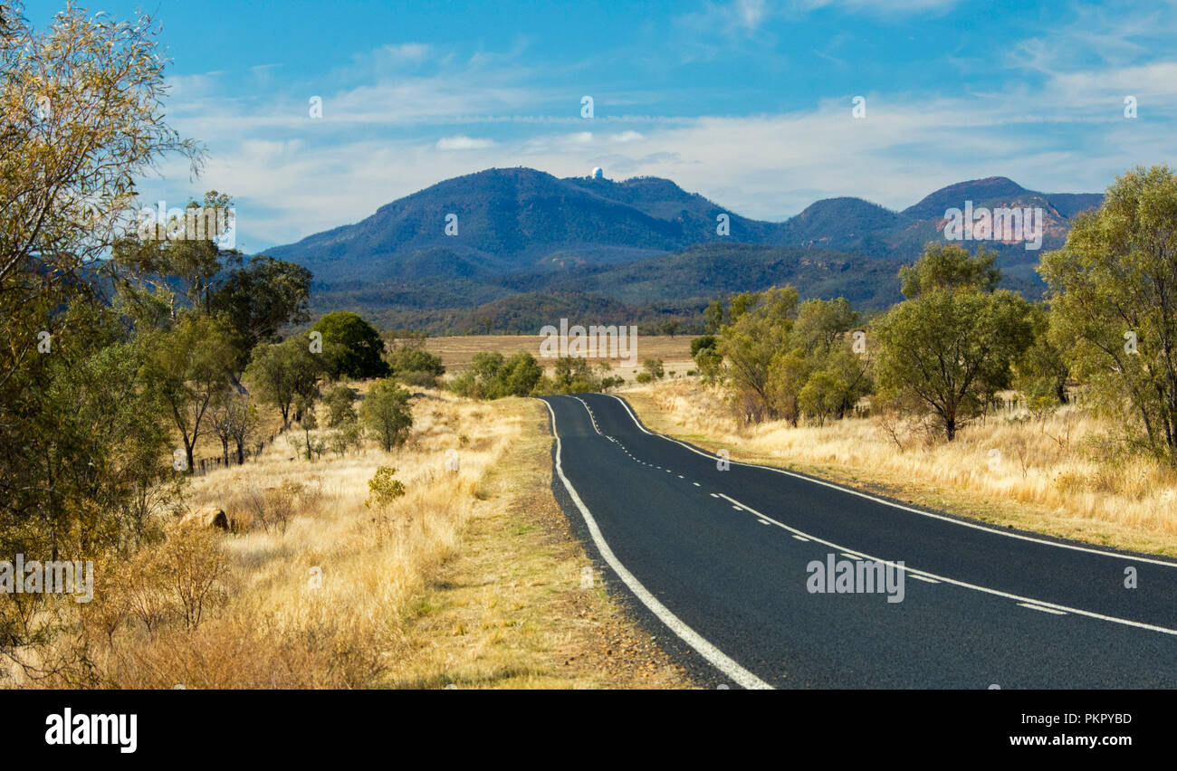 Paysage australien colorés avec route conduisant à travers les forêts et les herbes d'or à des pointes de Warrumbungle National Park s'élevant dans le ciel bleu dans le NSW Banque D'Images