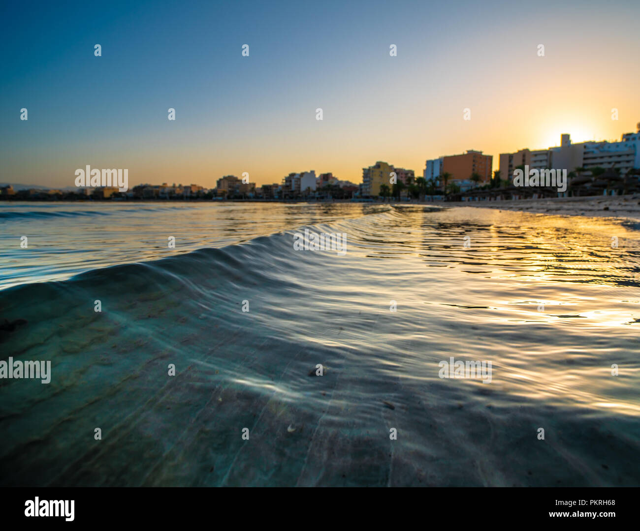 Des vagues d'or de la mer et ville à l'horizon pendant le coucher du soleil Banque D'Images