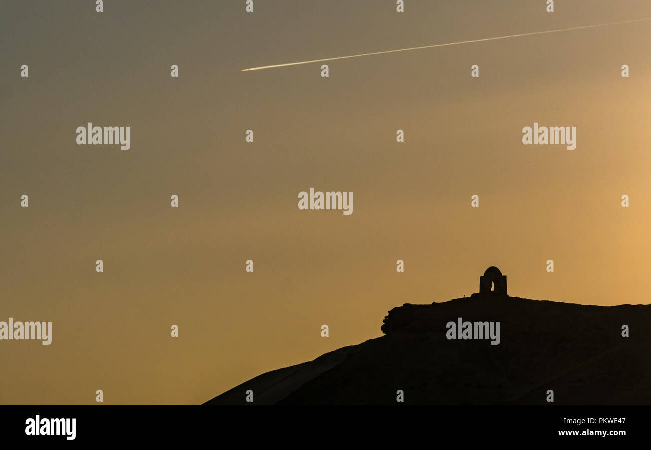 Vue de nuit sur la colline Qubbet el Hawa tombe, dôme du vent, avec avion jet de vapeur dans le sentier orange ciel dans crépuscule soir lumière, Assouan, Egypte, Afrique du Sud Banque D'Images