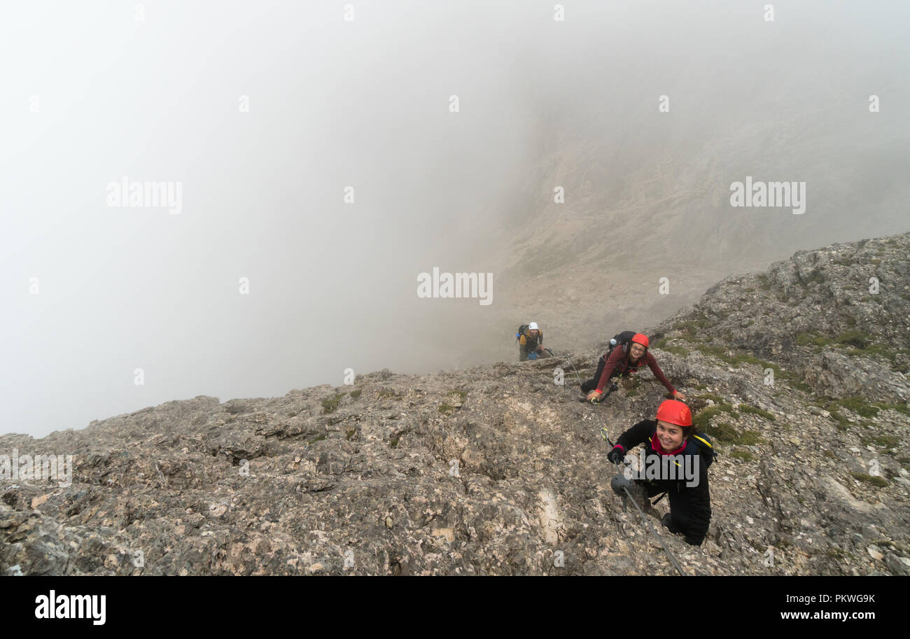 Trois jeunes attractive male et femelle d'alpinistes sur une pente raide et exposé Via Ferrata en Alta Badia dans le Tyrol du Sud dans les Dolomites italiennes Banque D'Images