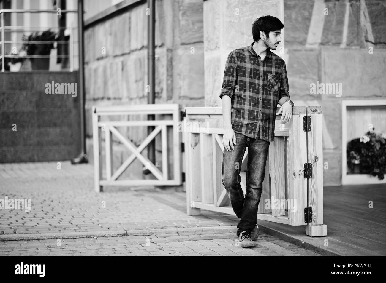 Jeune étudiant indien à l'homme rouge à carreaux shirt et jeans posés à ville. Banque D'Images