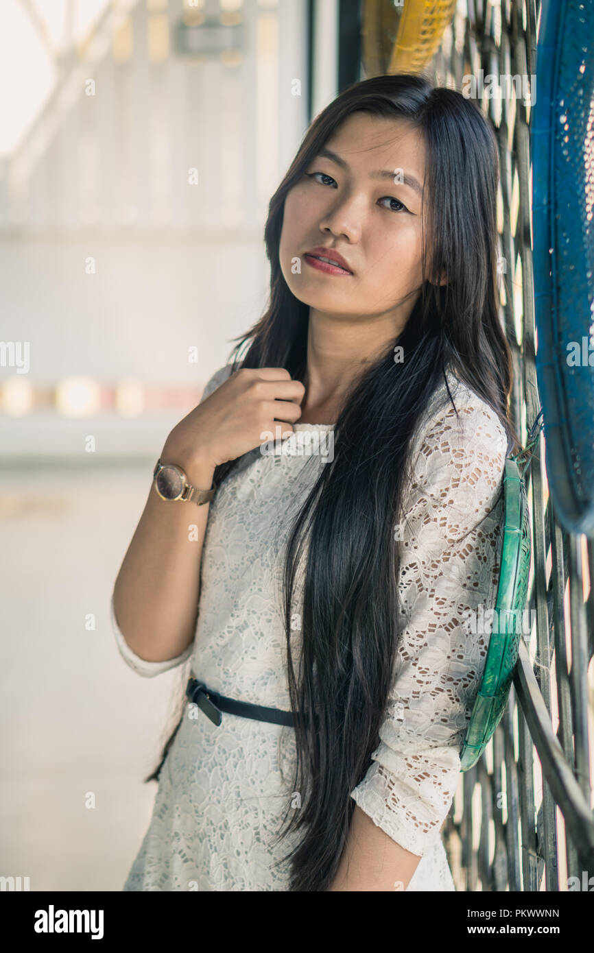 Jeune fille aux cheveux longs qui pose pour l'appareil à proximité d'un mur de bambou. Banque D'Images