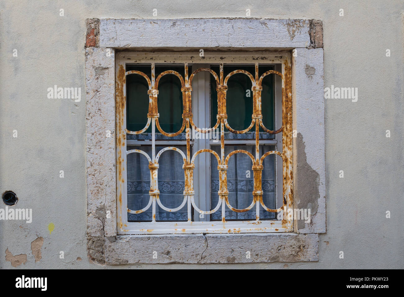 Petite fenêtre d'une vieille maison avec un cadre blanc, grille rouillée et rideaux blancs traditionnels. Centre ville de ville Krk, île de Krk, Croatie. Banque D'Images