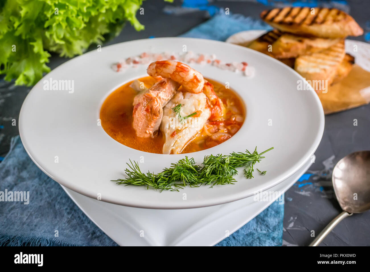 Soupe de poisson française Bouillabaisse aux fruits de mer, filet de saumon, crevettes, saveur riche, délicieux dîner dans un beau plat blanc Banque D'Images