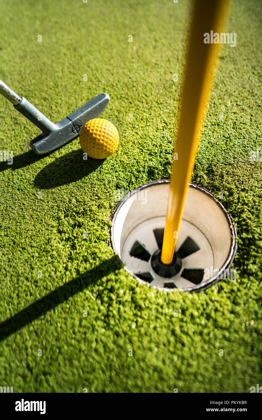 Mini-golf balle jaune avec un bâton près du trou au coucher du soleil Banque D'Images