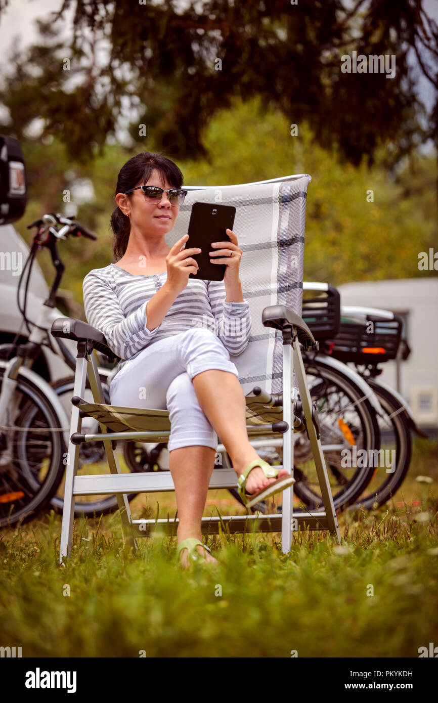 Femme regardant la tablette à côté du camping . Location caravane Vacances. Vacances famille vacances, voyages voyage en camping-car. Informations de connexion wi-fi Banque D'Images