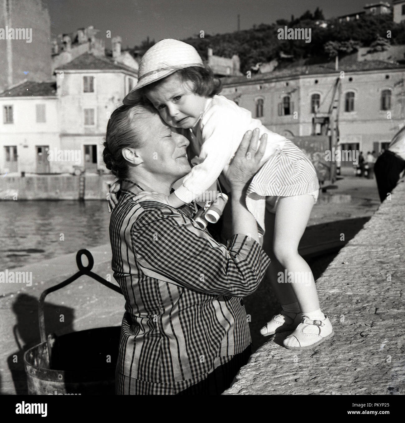 Années 1950, historique, par un petit port, une grand-mère détient et le confort d'une petite fille en détresse qui pensent qu'elle a été perdu, de l'Italie. Banque D'Images