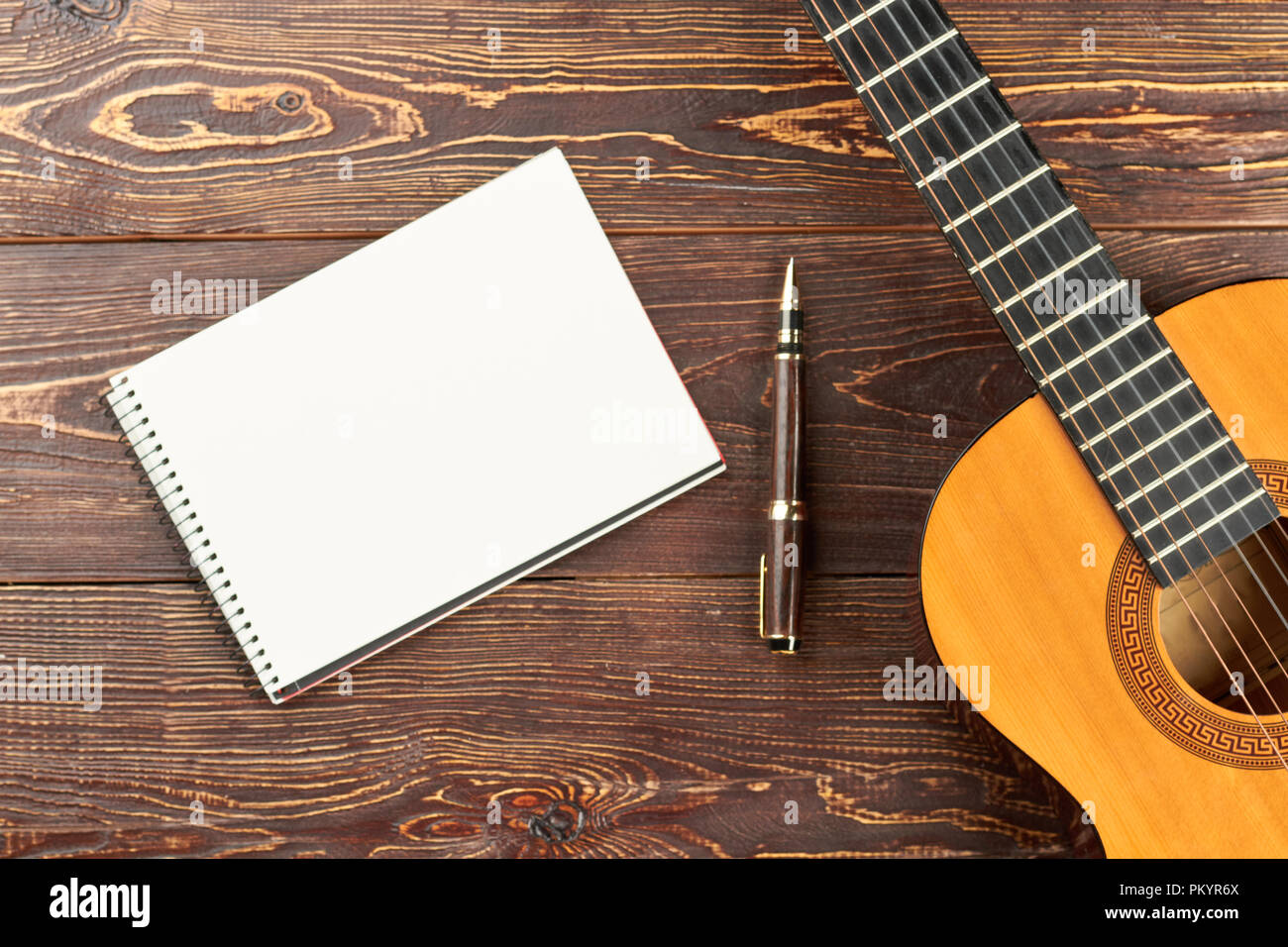 La guitare avec blank carnet et un stylo. Espace de travail avec ordinateur portable blanc, stylo et guitare acoustique sur fond de table en bois brun. L'espace de travail de l'auteur-compositeur. Banque D'Images