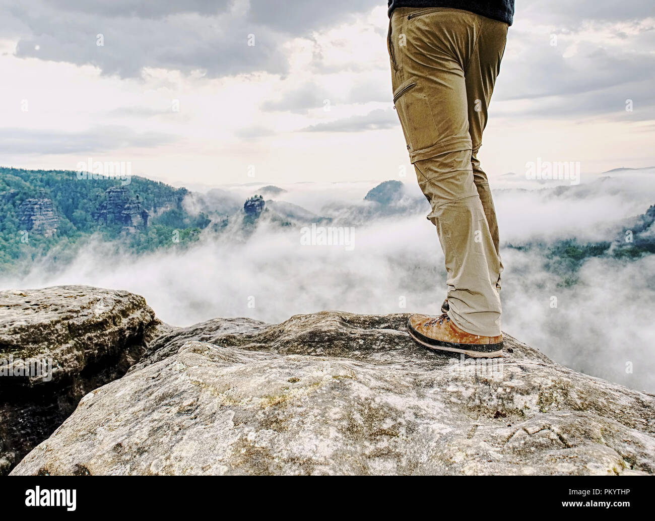 Randonneur avec jambes homme pantalon coupe-vent et des bottes de randonnée sur sommet de montagne roche avec une vallée à l'arrière-plan Banque D'Images
