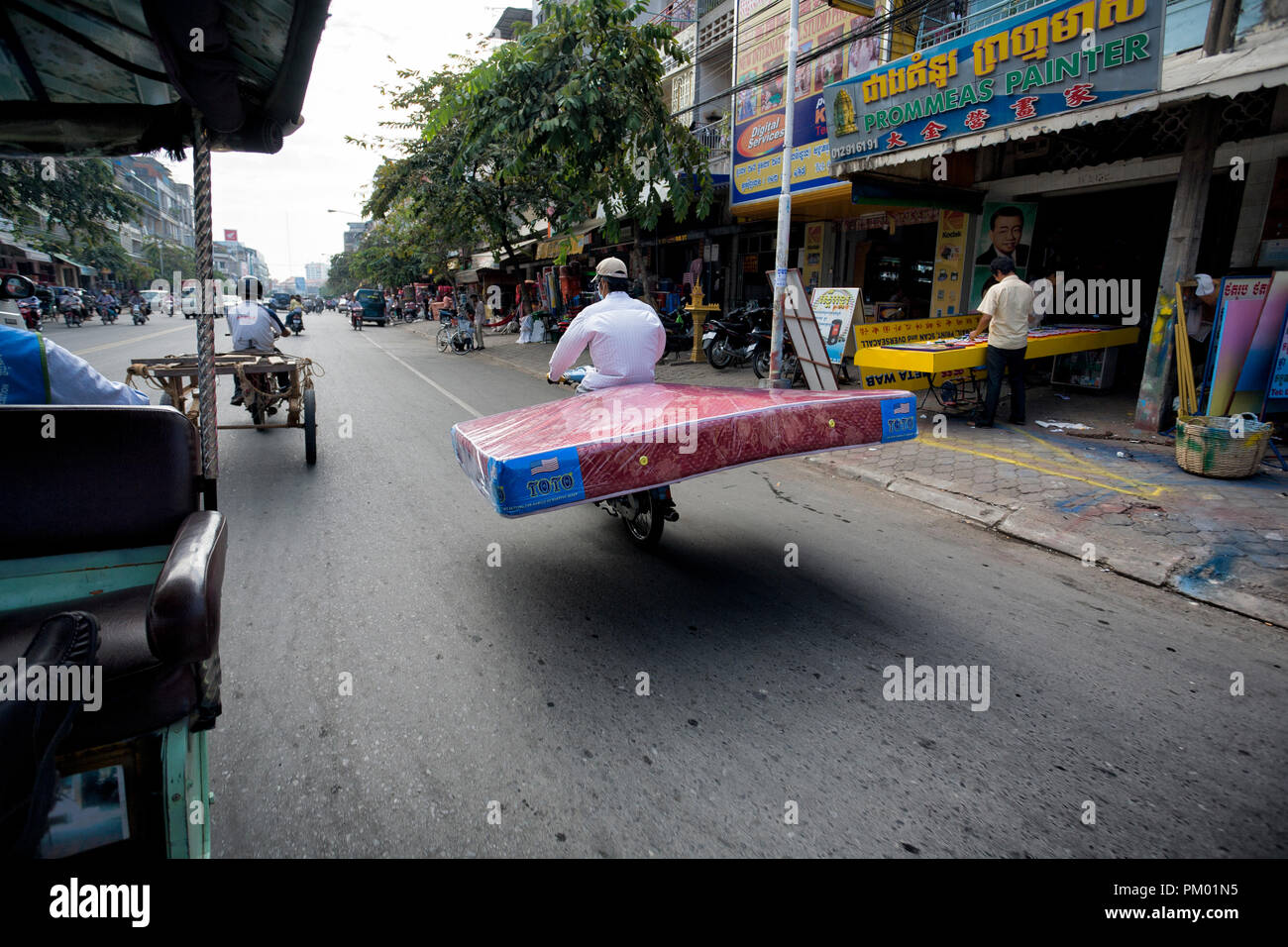 Charge non sécuritaires. Le Cambodge. Phnom Penh. Man riding une moto et le transport d'un grand lit double matelas. Banque D'Images