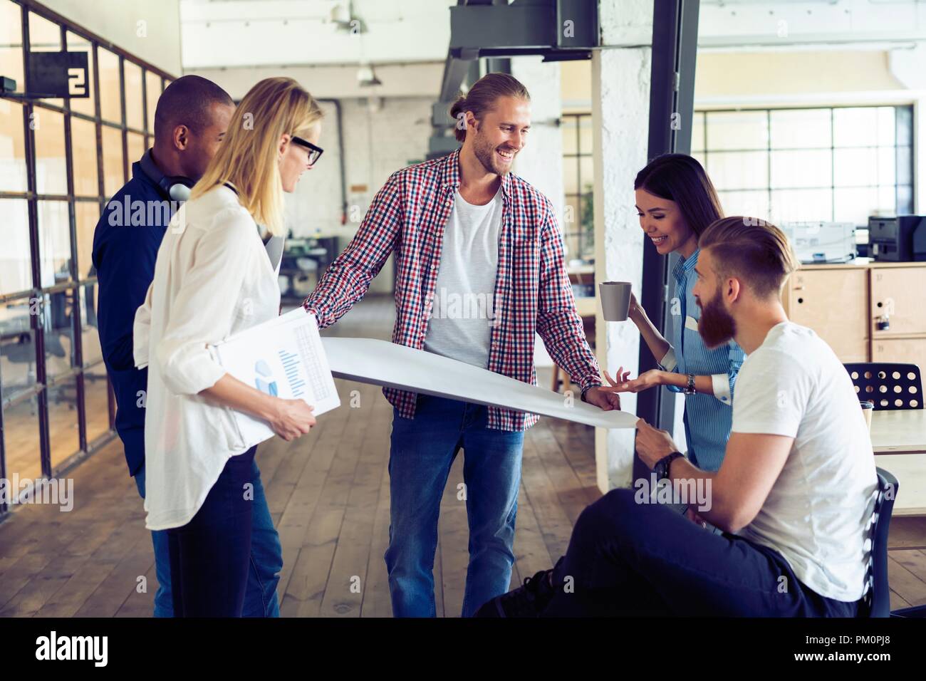 Travailler en équipe. Longueur totale de jeunes gens modernes dans smart casual wear planning business stratégie alors que jeune femme pointant sur grand papier dans le couloir. bureau Banque D'Images