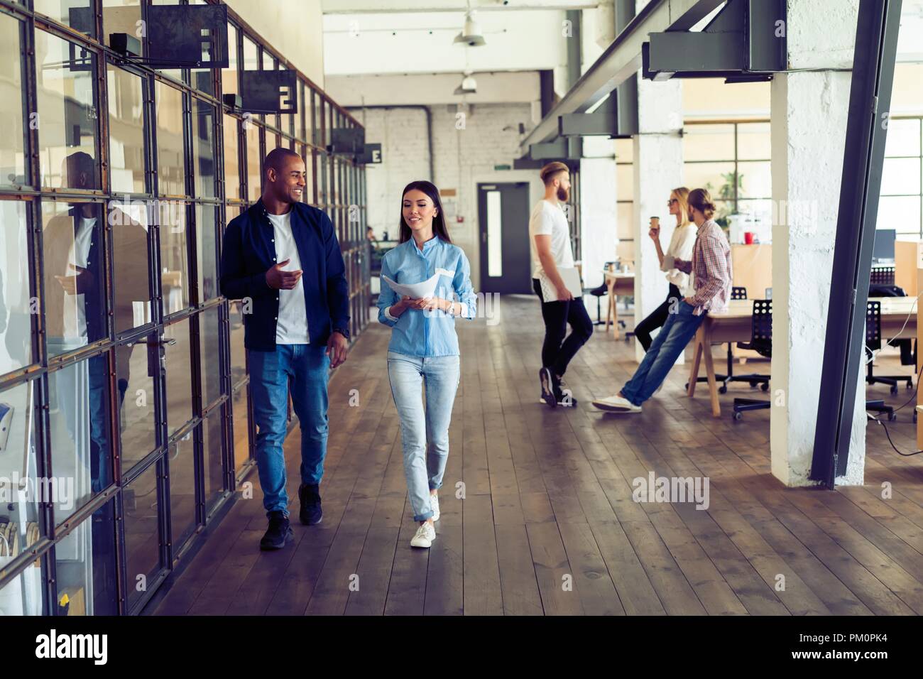 Rattrapage avant la réunion. Longueur totale de jeunes gens modernes dans smart casual wear discuter affaires et souriant tout en marchant à travers le corridor. Banque D'Images