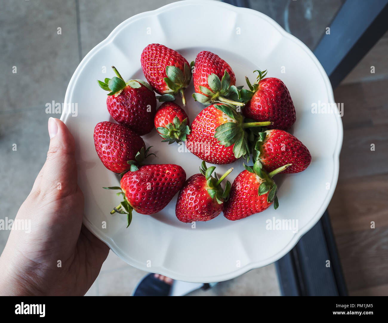 Fraises rouges frais sur plaque blanche avec holding hand Banque D'Images