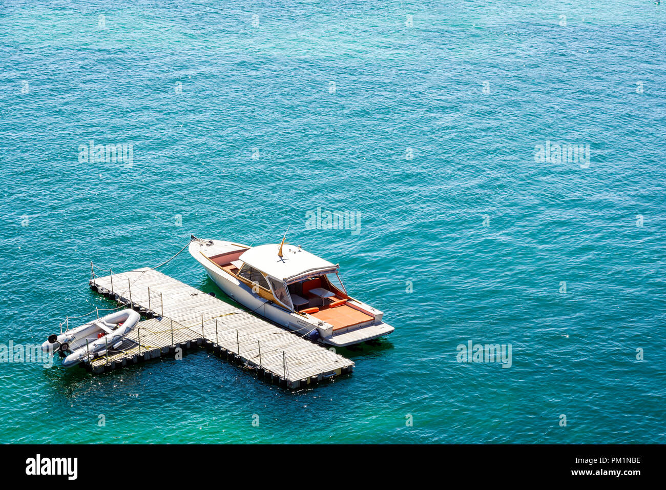 Un luxueux bateau amarré à une forme en t, isolés, en station d'eaux vert avec une annexe gonflable portant sur le dock. Banque D'Images